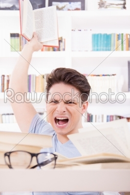 angry student with expression surrounded by books  throwing a bo