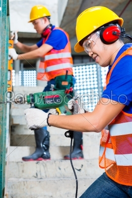 Asian construction workers drilling in building walls
