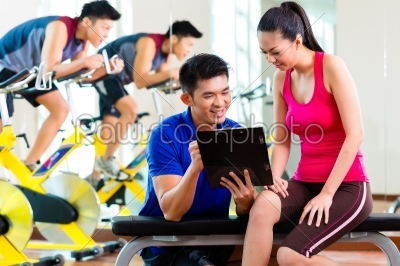 Asian personal trainer with woman in fitness gym