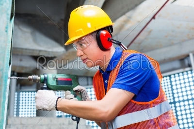 Asian worker drilling in construction site wall