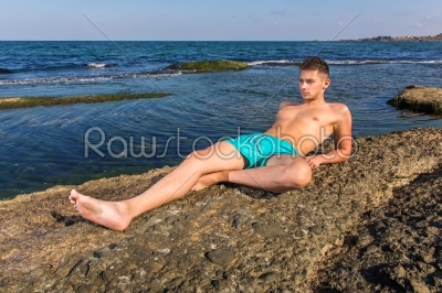 Attractive handsome sexy naked young man on rock near the sea