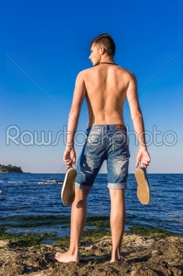 Attractive handsome sexy naked young man on rock near the sea
