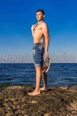Attractive handsome sexy naked young man on rock near the sea wa