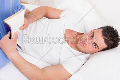 attractive man in pajamas lying on the bed reading book