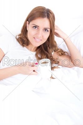 Attractive woman with a cup of coffee on the bed