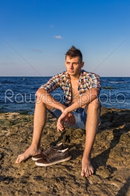 Attractive young fashion sexy man on rock near the sea water