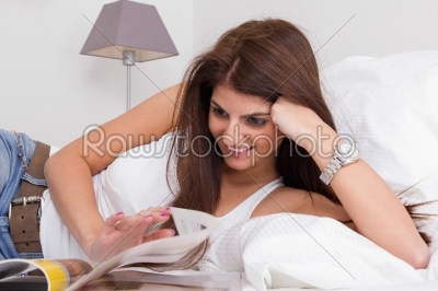 beautiful young woman on the bed reading magazine