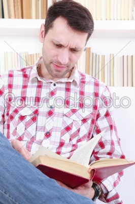 casual young man reading a novel book while relaxing on sofa