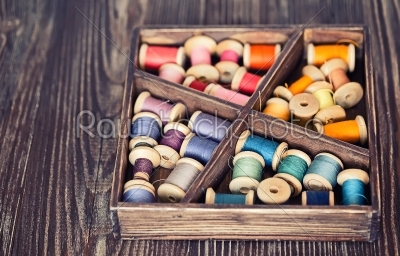 Collection of different color spools  threads  arranged in a grunge wooden box