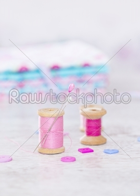 Collection of spools  threads in pink colors arranged on a white wooden background
