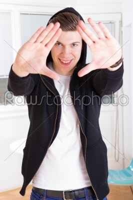 cool young guy in hooded jacket framing his face with hands