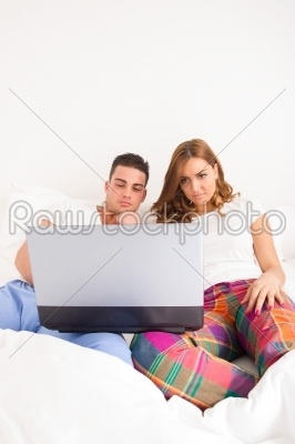 couple sitting side by side in bed relaxing with computer