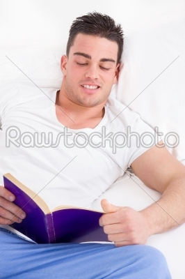 gorgeous man reading book in bed smiling