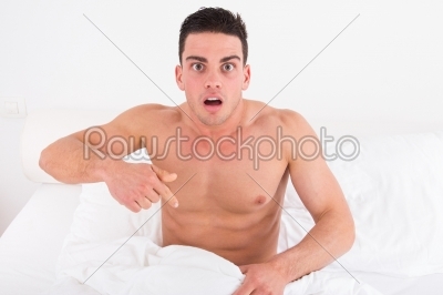 half naked young man in bed  looking down at his underwear at hi