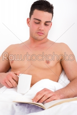 man in bed drinking coffee and reading in the morning