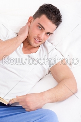 man with neck pain reading book in bed