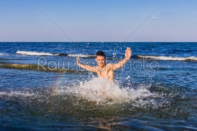 Naked young man jumping for joy from see water
