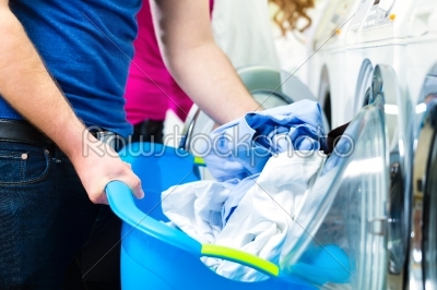 People in a launderette, washing their dirty laundry, in the background are washing machines