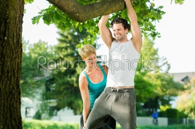 People in city park doing chins or pull ups on tree