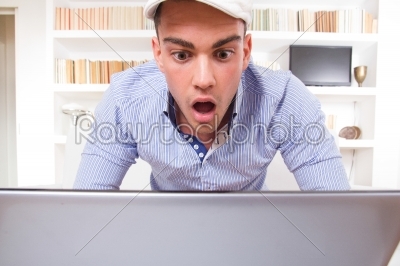 portrait of a shocked male student looking at monitor of his lap