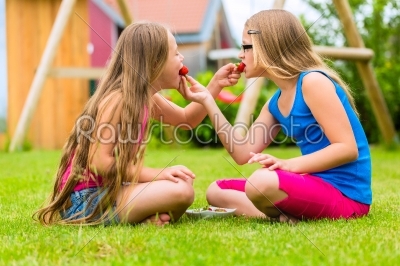 sisters playing in garden eating strawberries