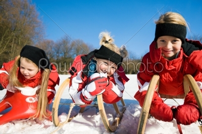 Three children with toboggan in the snow