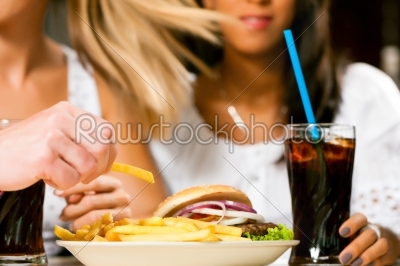 Two women eating hamburger and drinking soda