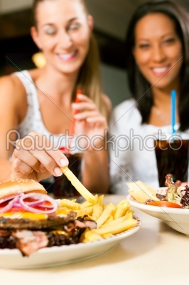 Two women eating hamburger and drinking soda