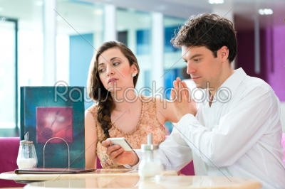 Young couple in cafe not interacting but on phone