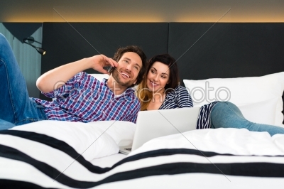 Young couple in Hotel in bed with phone and computer
