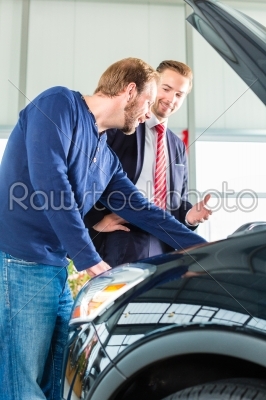 Young man and seller with auto in car dealership