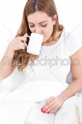 young woman enjoying reading and drinking coffee in bed