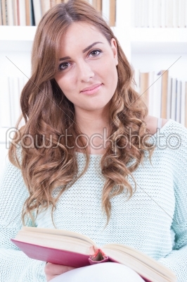 young woman or student reading a book while sitting on a sofa